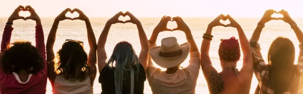 Photo of a group of women facing away from the camera with their hands raised above their heads making a heart with their hands